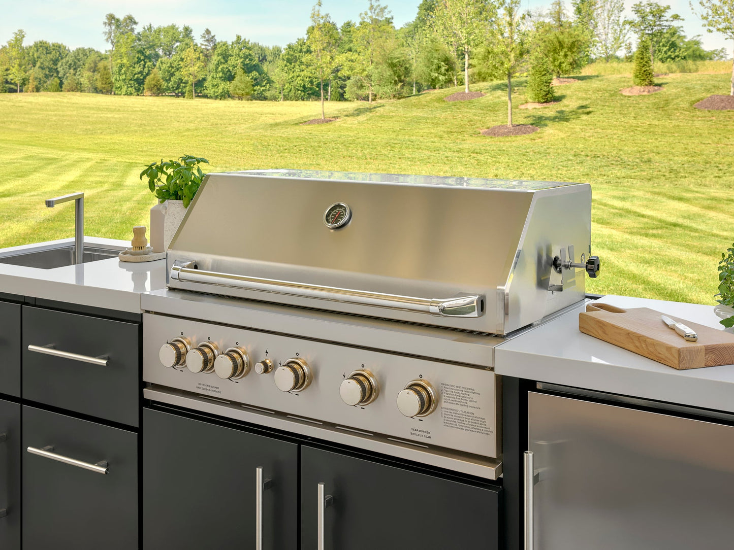 Stainless steel Emory outdoor grill with temperature gauge and control knobs built into cabinetry with white countertop.