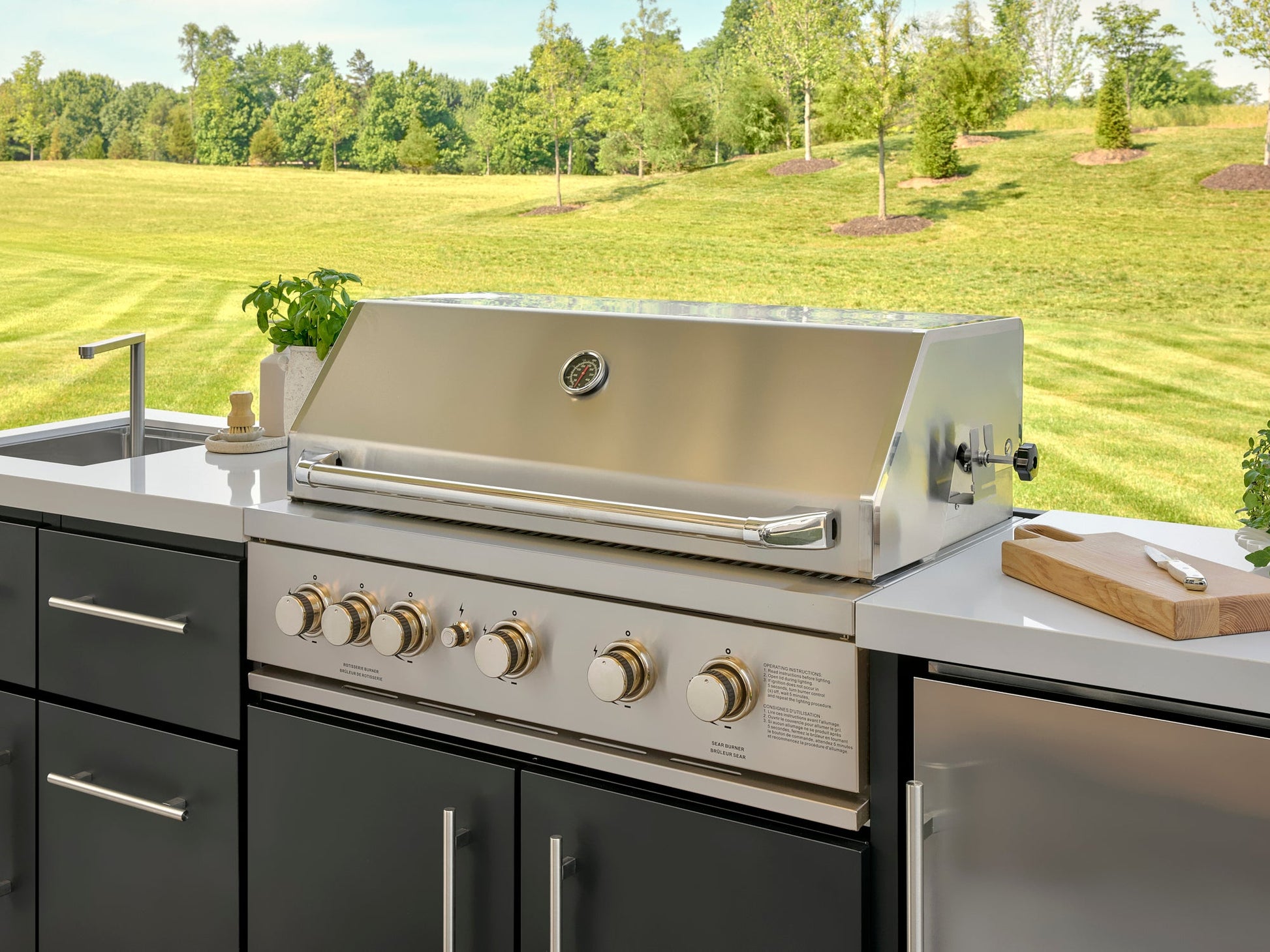 Stainless steel Emory outdoor grill with temperature gauge and control knobs built into cabinetry with white countertop.