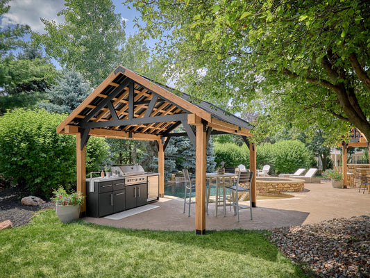 Steel pavilion gazebo with exposed wood-look beams creating backyard shade over outdoor kitchen, bar seating, and pool patio.