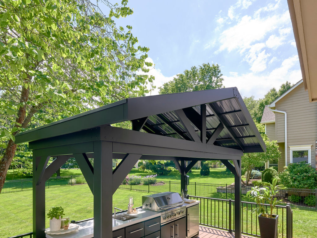 Range Outdoor Living Lancaster outdoor kitchen with steel roof and premium grill in landscaped backyard setting.