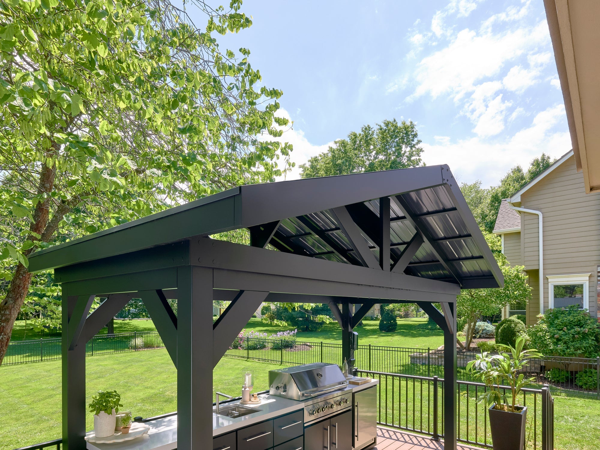 Range Outdoor Living Lancaster outdoor kitchen with steel roof and premium grill in landscaped backyard setting.