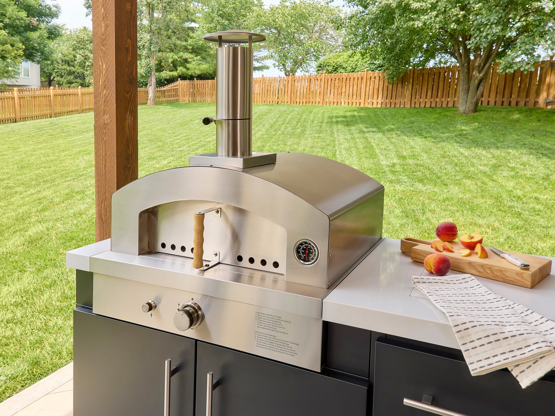 Built-in pizza oven with temperature gauge on Emory outdoor kitchen island with countertop and wood cutting board.