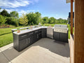L-shaped Emory backyard kitchen with dark cabinets, engineered stone countertop, built-in grill, and refrigerator on patio.