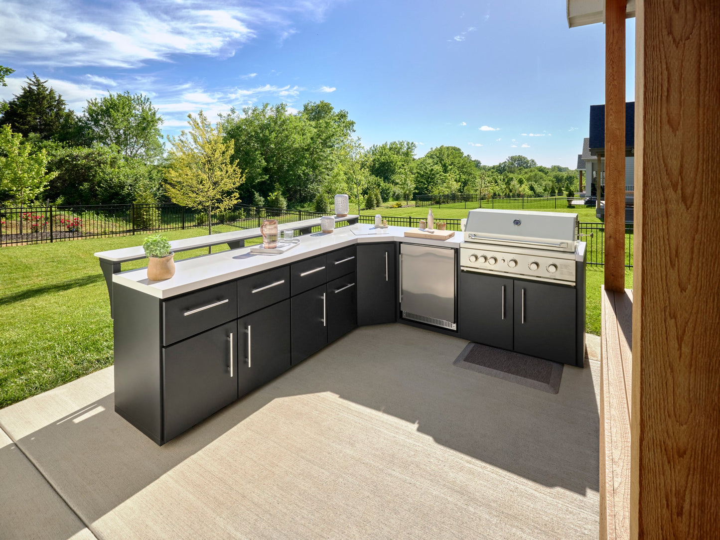 L-shaped Emory backyard kitchen with dark cabinets, engineered stone countertop, built-in grill, and refrigerator on patio.