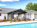 Dark gray Lancaster hardtop gazebo with dining table beside pool and white house with landscaping under blue sky.