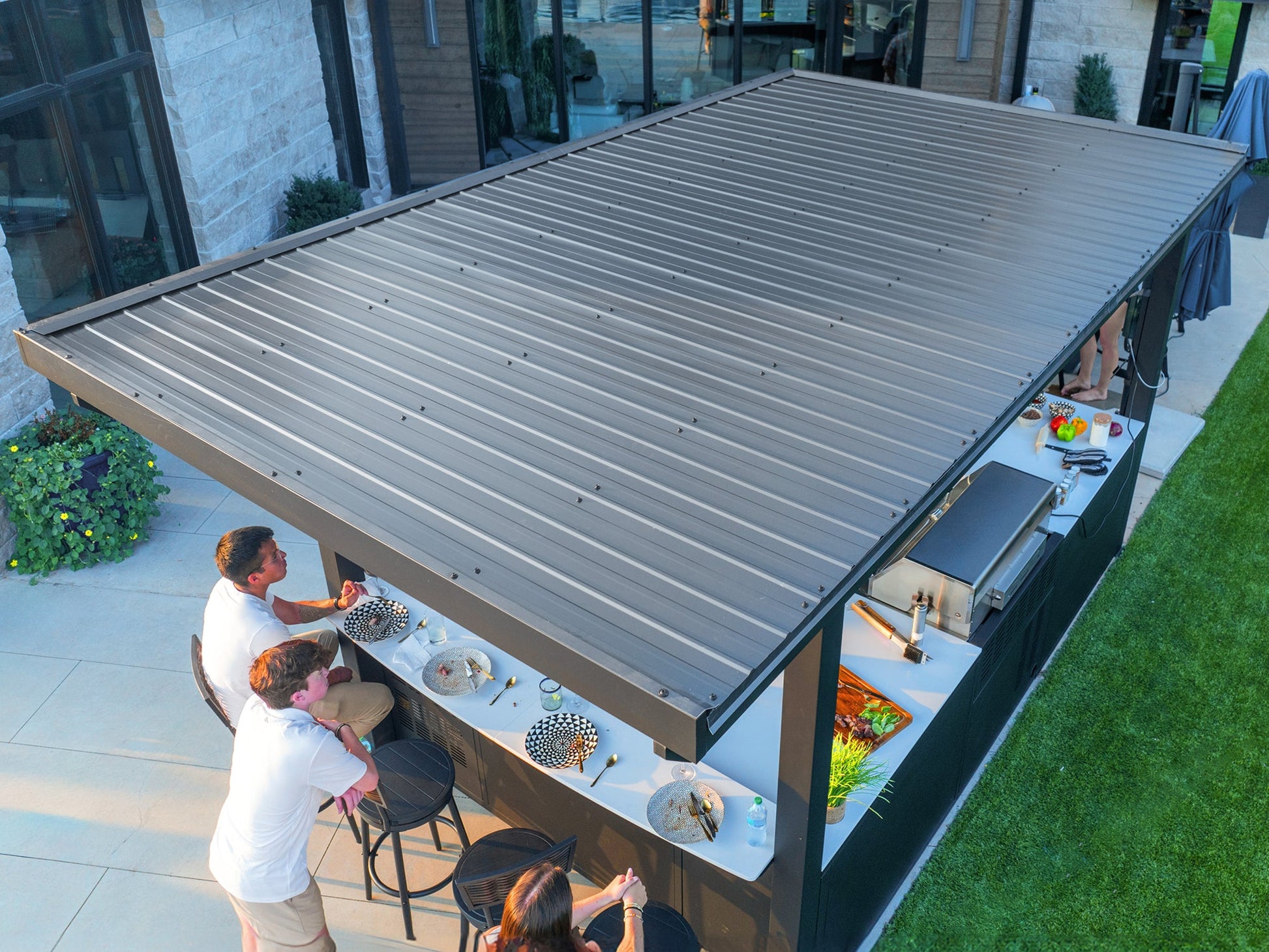 Edgemont Bay outdoor kitchen top view with galvanized steel roof and guests enjoying space below.