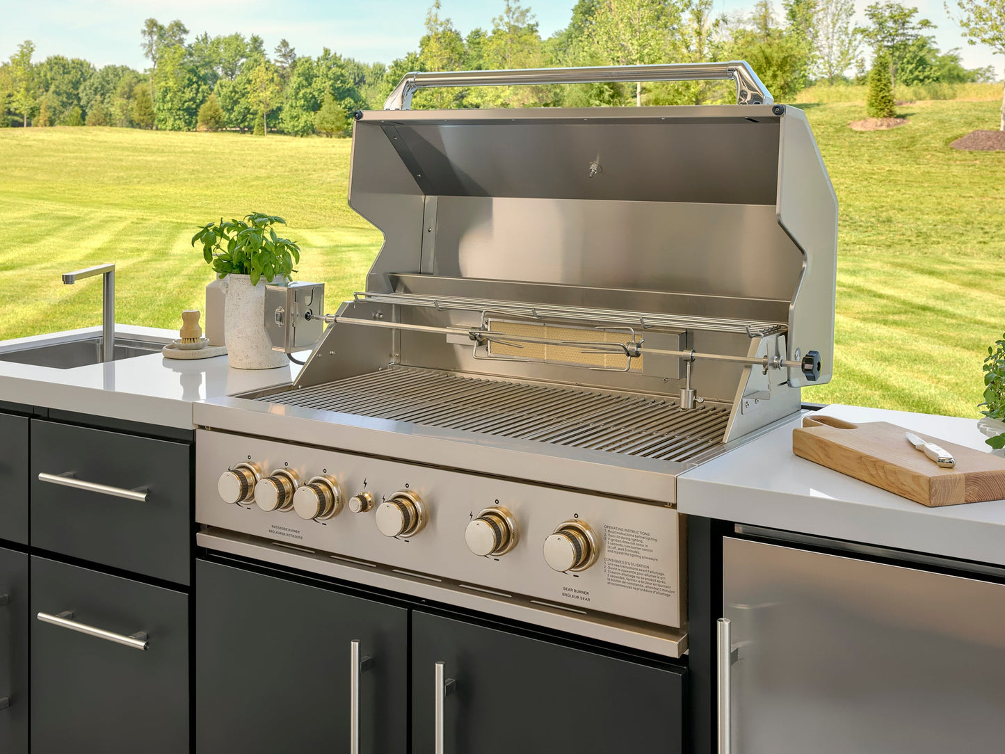 Open built-in grill with rotisserie and multiple control knobs in Emory outdoor kitchen with engineered stone countertop.