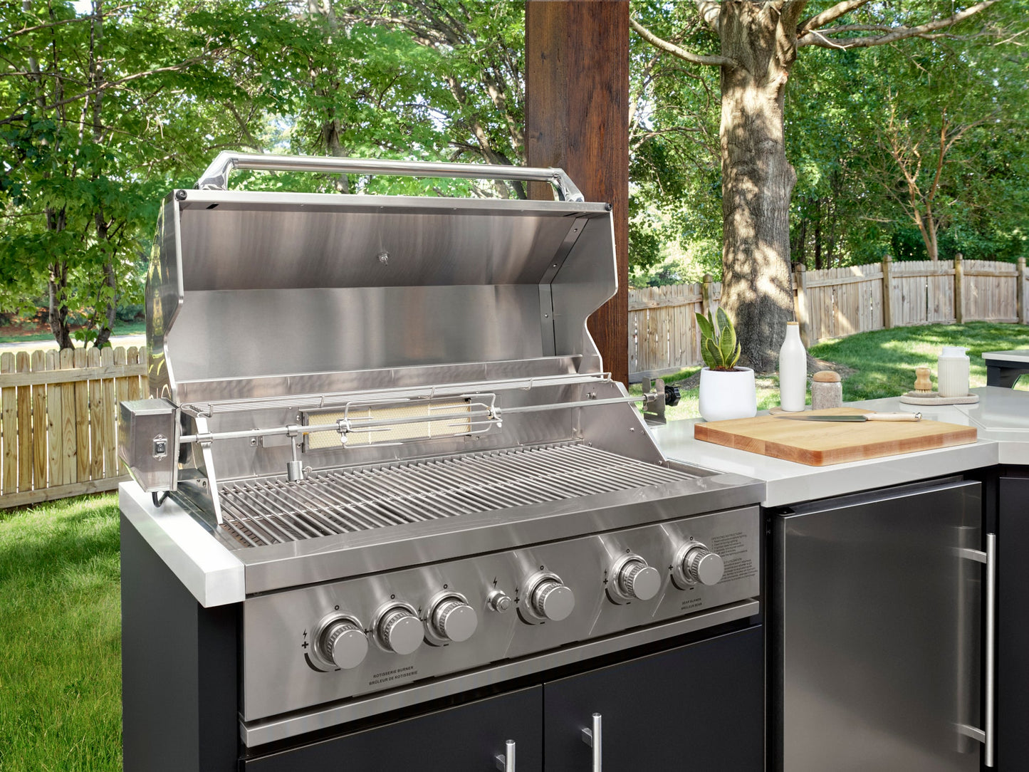 Open stainless steel patio grill with rotisserie and warming rack on Emory outdoor kitchen island with countertop.