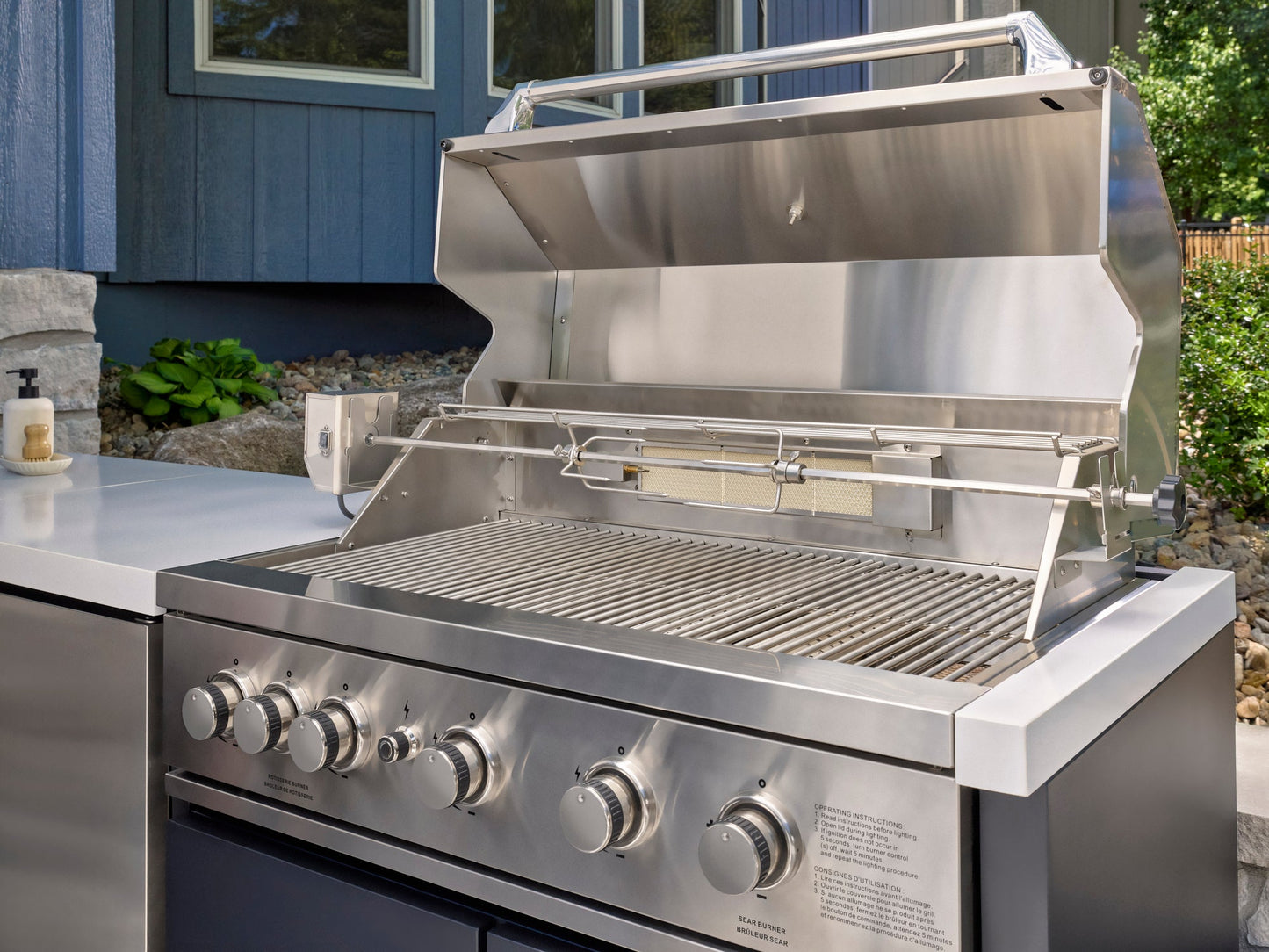 Emory built-in outdoor grill station with open stainless steel lid, rotisserie attachment.